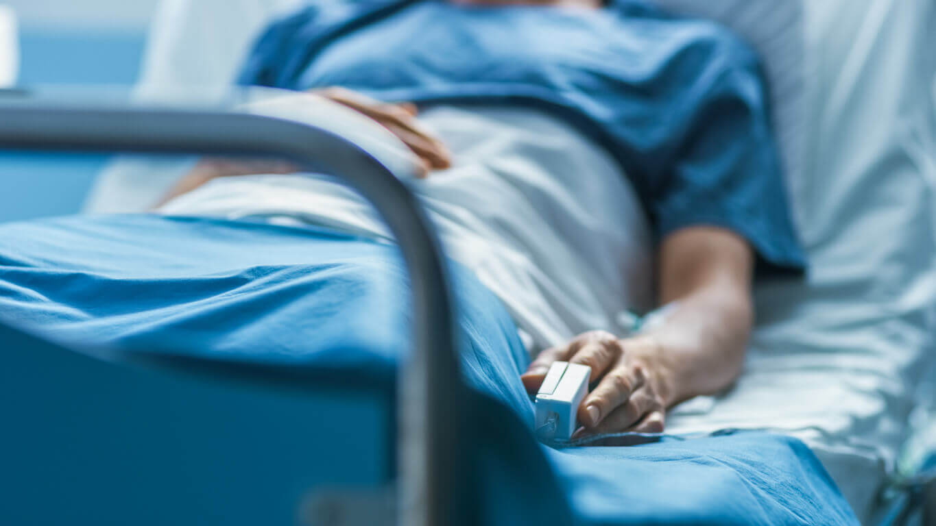 A patient laying in a hospital bed with a heart rate monitor no their finger. 